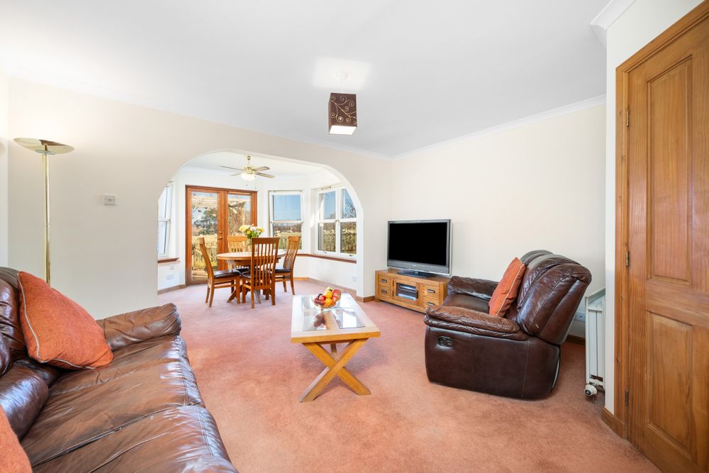 Modern living room interior with leather recliners, wooden floor, and glass doors leading to dining area.