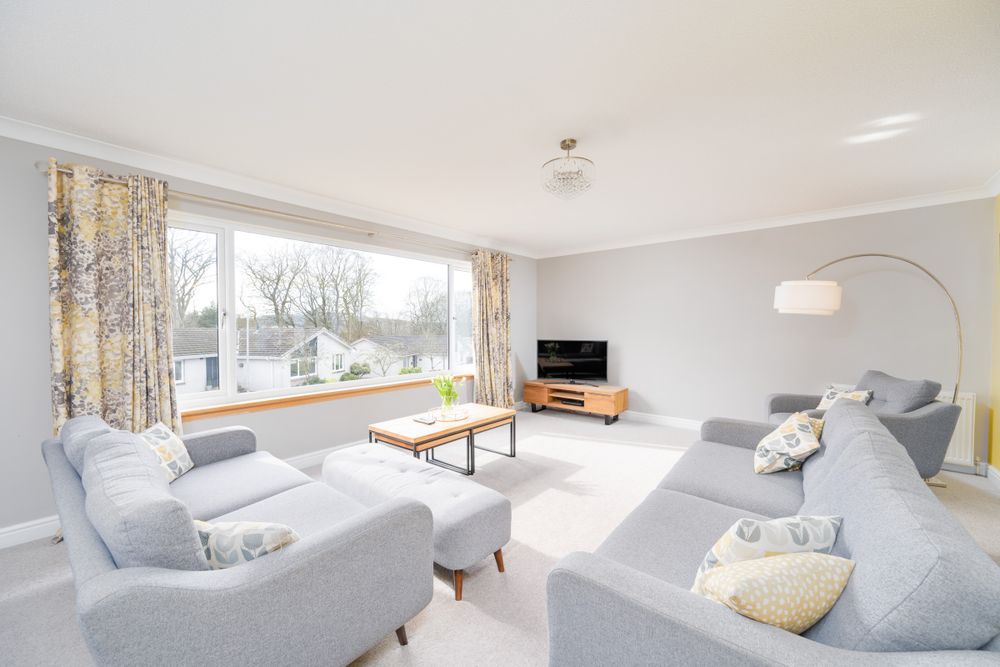 Bright modern living room with light gray sofas, floral curtains, and large window overlooking snowy winter landscape.