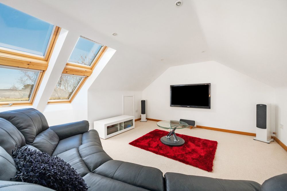 Modern attic living room with black leather sofa, wall-mounted TV, red rug and skylights flooding natural light into space.