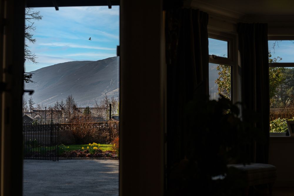 Dark interior room with window view of mountains and buildings silhouetted against blue sky on bright autumn day.
