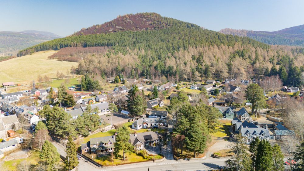 Aerial view of a small mountain town nestled among evergreen trees with hills and mountains in the background.