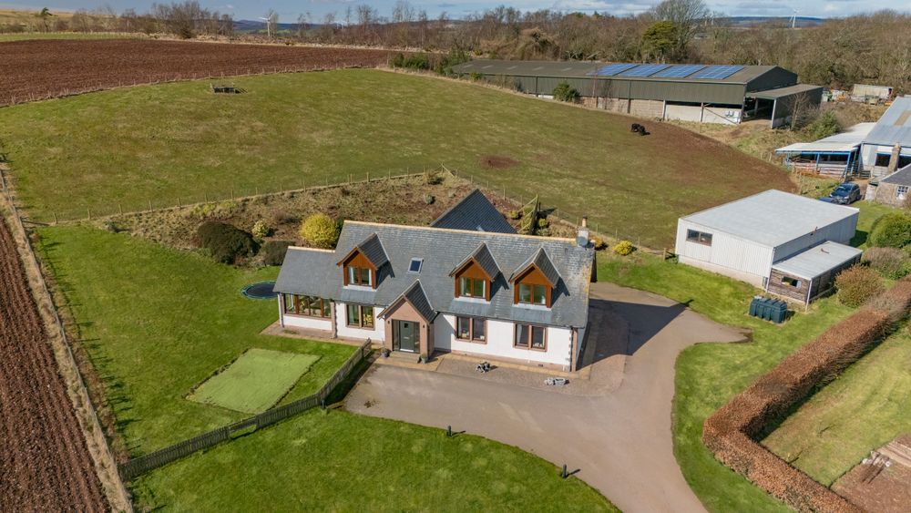 Aerial drone view of a modern gray house with dormers and large lawn in rural countryside setting.