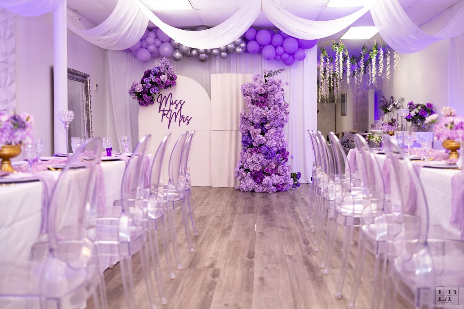 Elegant wedding venue decorated with purple lighting and white fabric draping from the ceiling.
