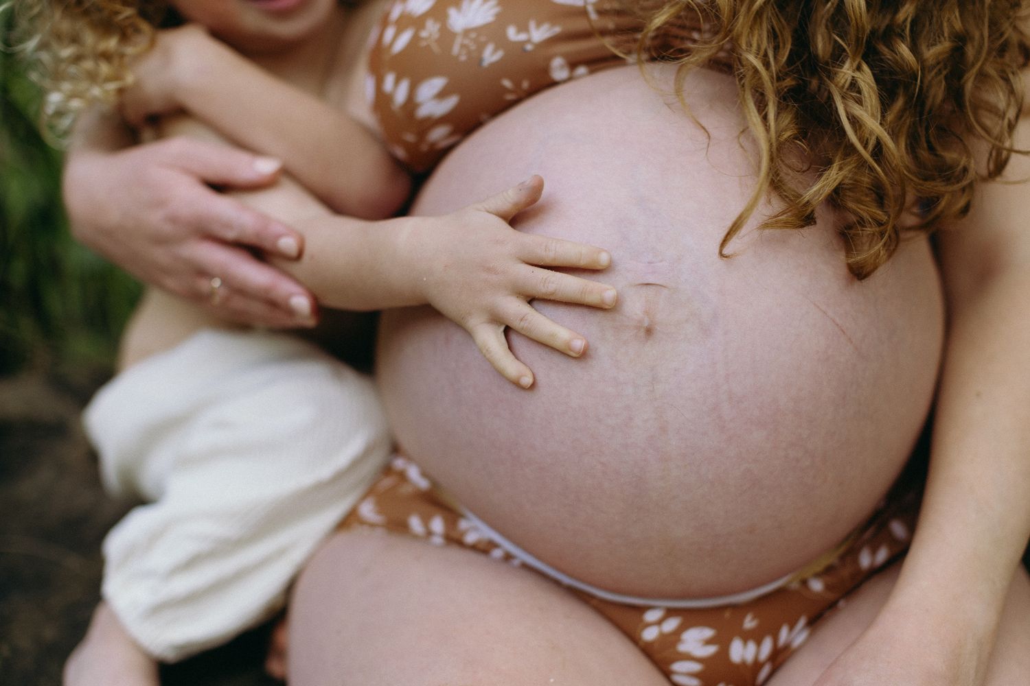 Close up of belly of pregnant woman in bikini. Toddler sons hand on her belly button.
