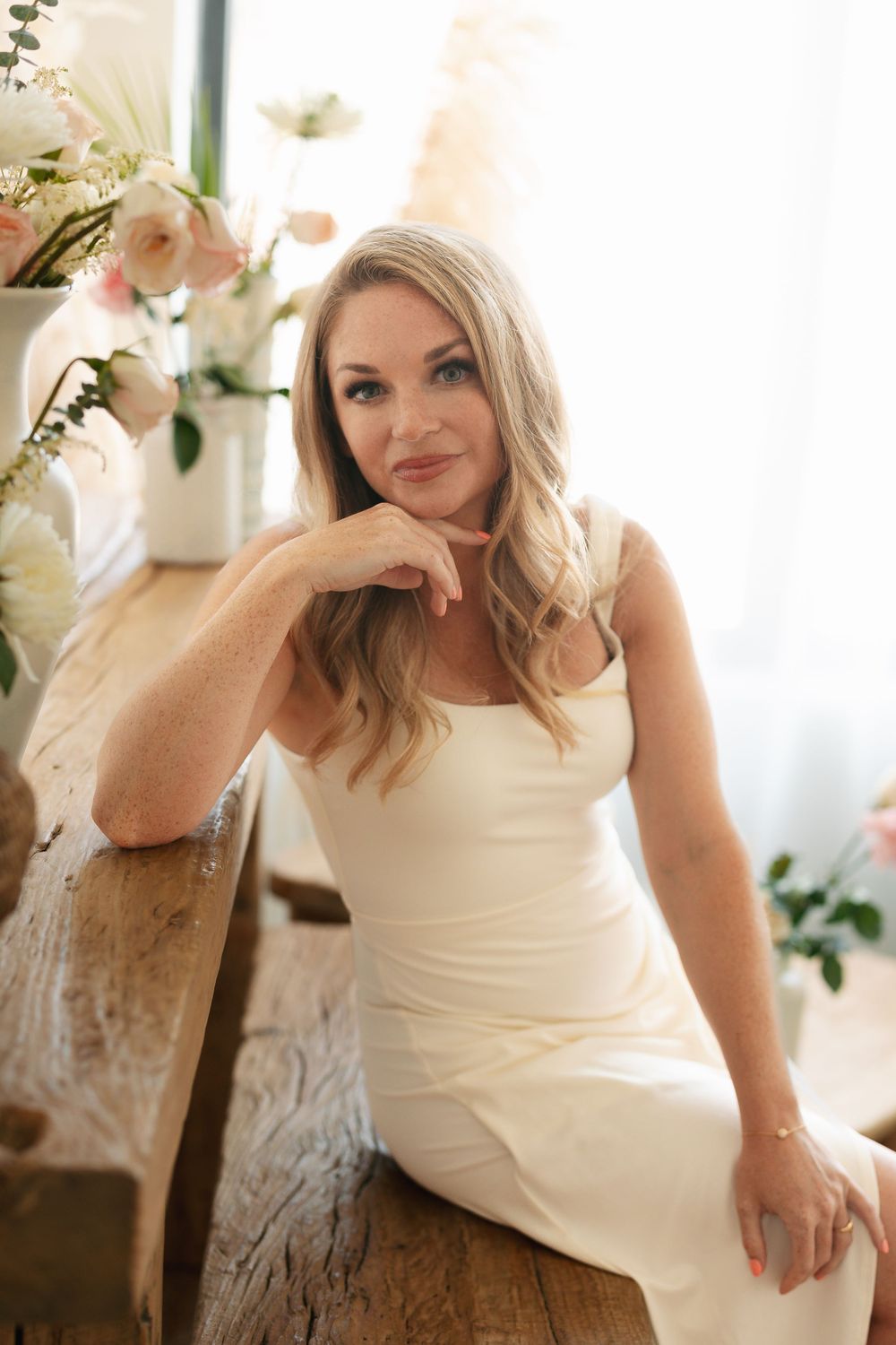 Soft romantic portrait with cream dress and floral decor in bright interior setting.