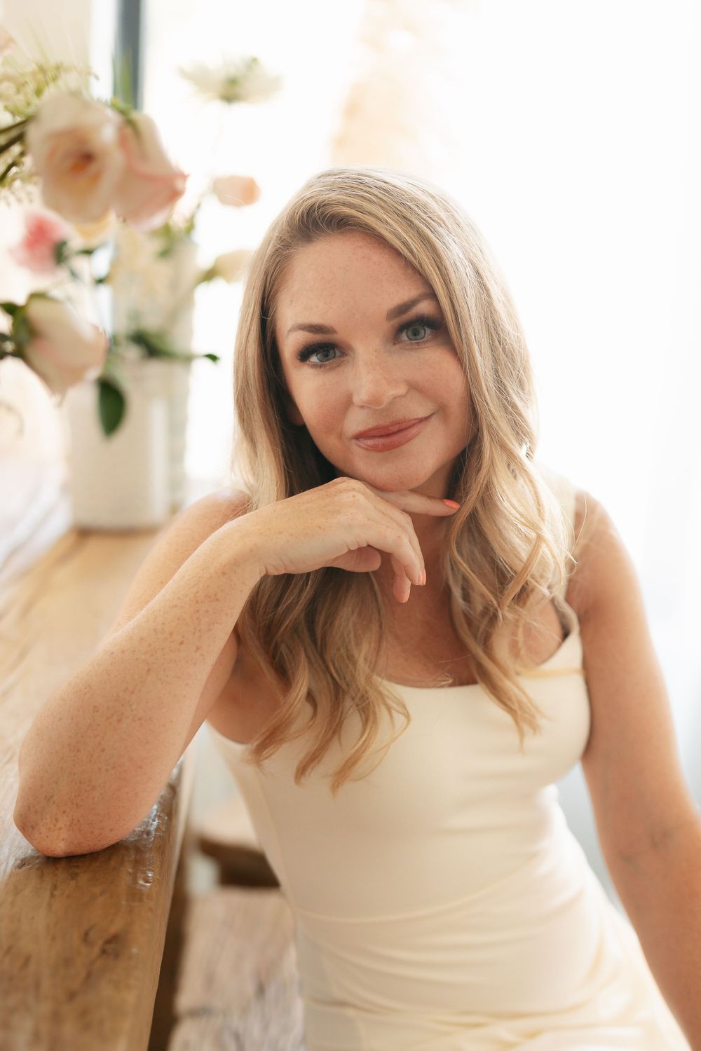 A relaxed portrait in a cream dress with natural light and floral decor in the background.