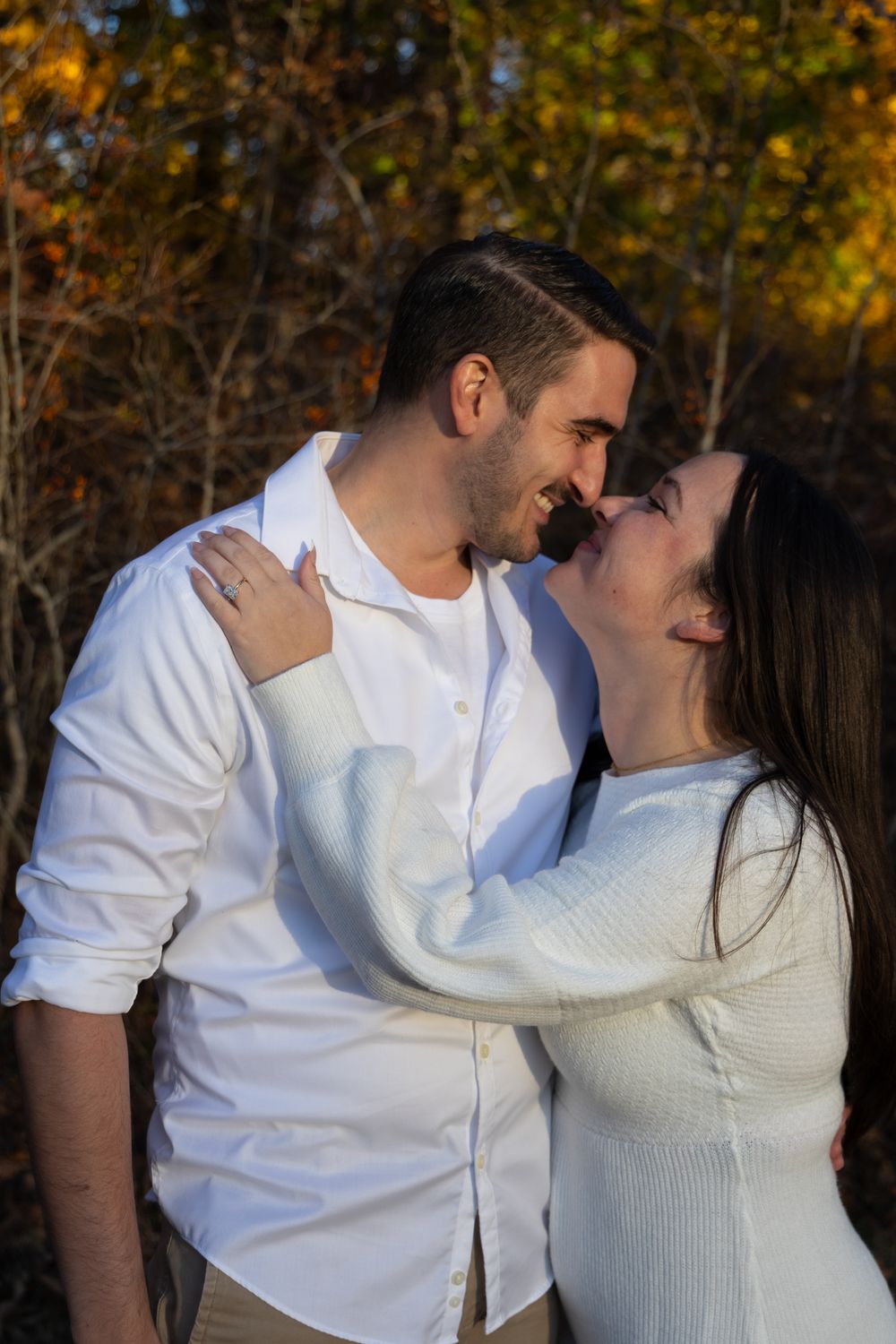 Romantic couple almost kissing outdoors, surrounded by colorful fall foliage in golden sunlight.