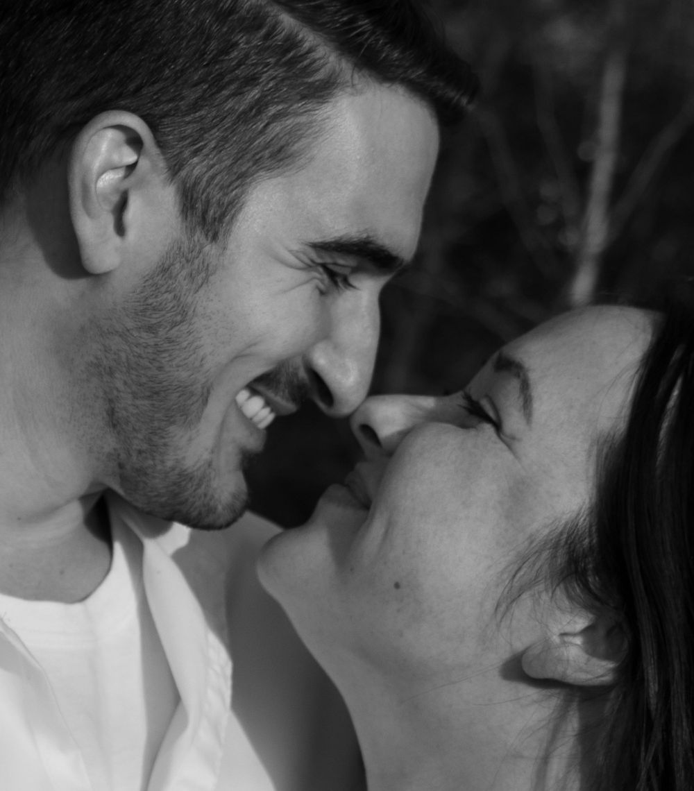 Black and white close-up of smiling couple almost kissing outdoors.