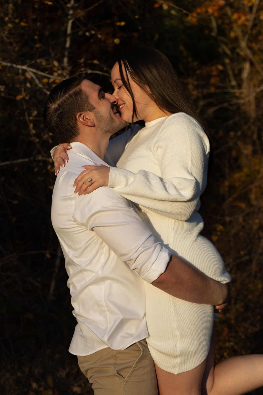 Romantic couple in white outfits nearly kissing while embracing in autumn setting.