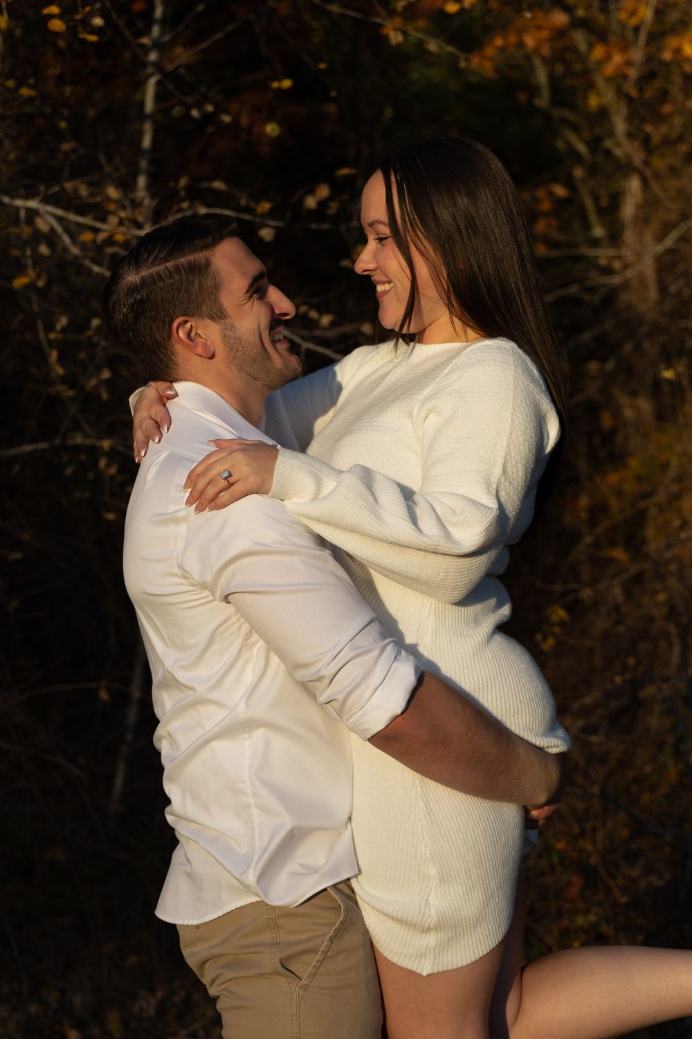 Happy couple laughing and embracing in warm autumn sunlight with fall foliage.