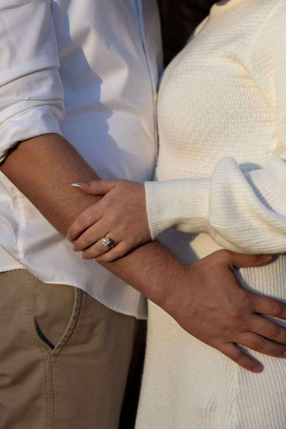 Close-up of couple's intertwined arms showing engagement ring in coordinating white outfits.