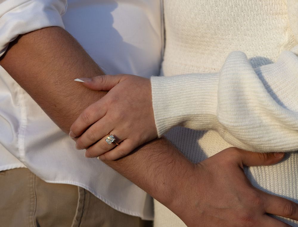 Close-up of couple holding hands showing engagement ring with white outfits.