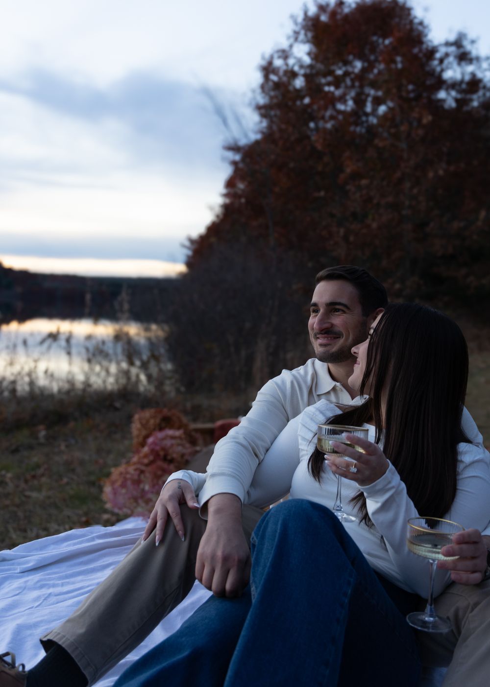 Couple sitting together on a blanket enjoying wine while gazing at a scenic autumn lake sunset.