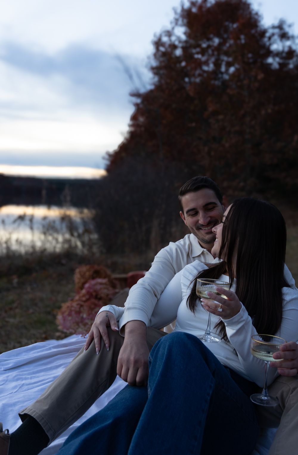 Happy couple cuddling and sharing a laugh during a romantic lakeside picnic at sunset.