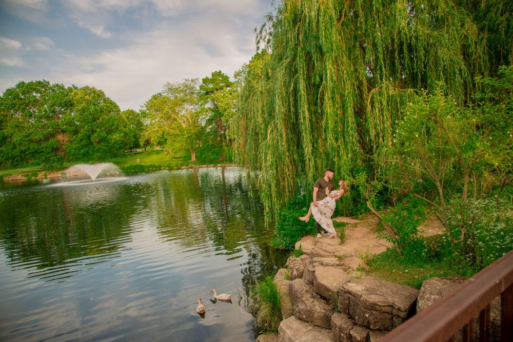 Young woman sitting on rocks by a scenic pond under a weeping willow tree with ducks swimming nearby.