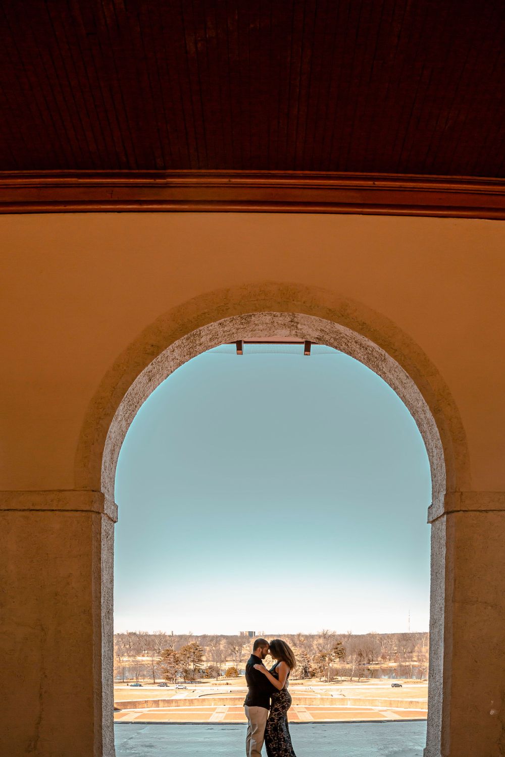 Couple silhouetted in romantic embrace framed by elegant stone arch with scenic outdoor view.