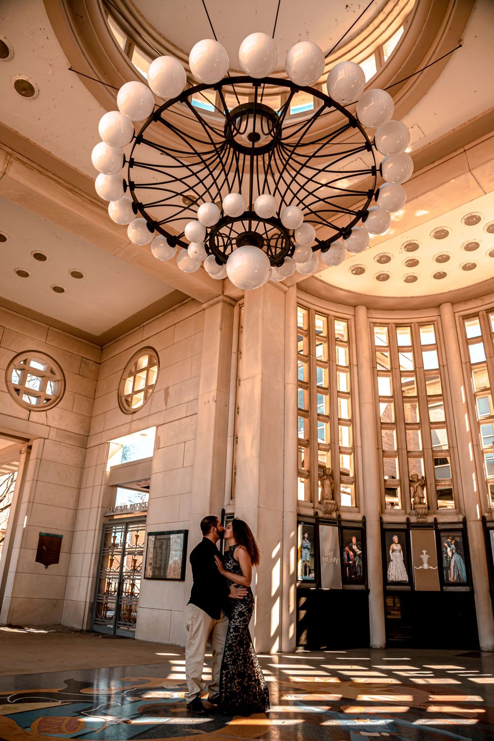 Couple sharing a romantic kiss under an elegant chandelier in a stunning grand architectural interior.