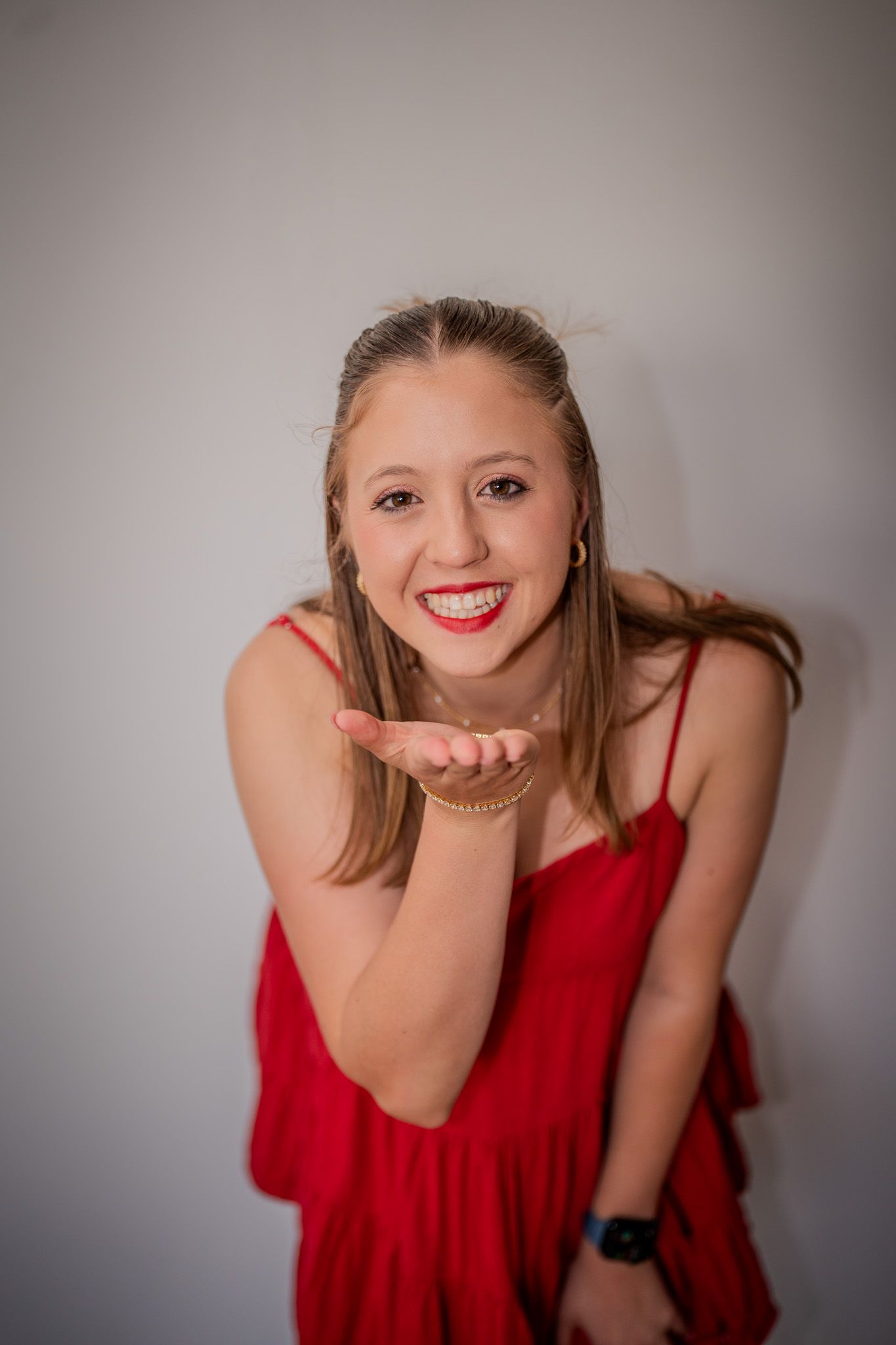 Someone in a red dress blows a kiss while posing against a gray wall.
