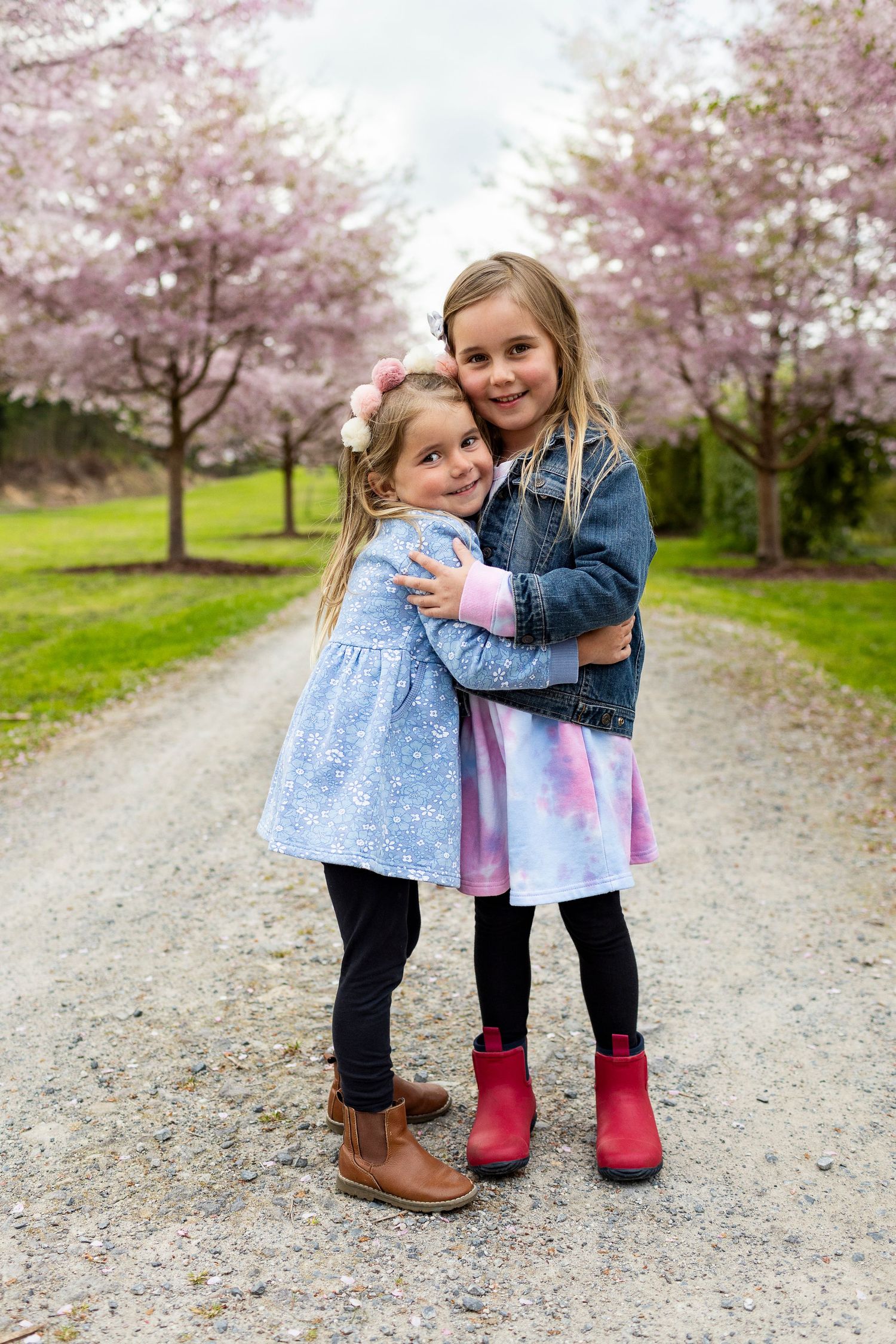 Two children embrace on a gravel path under blooming pink cherry blossom trees in springtime.