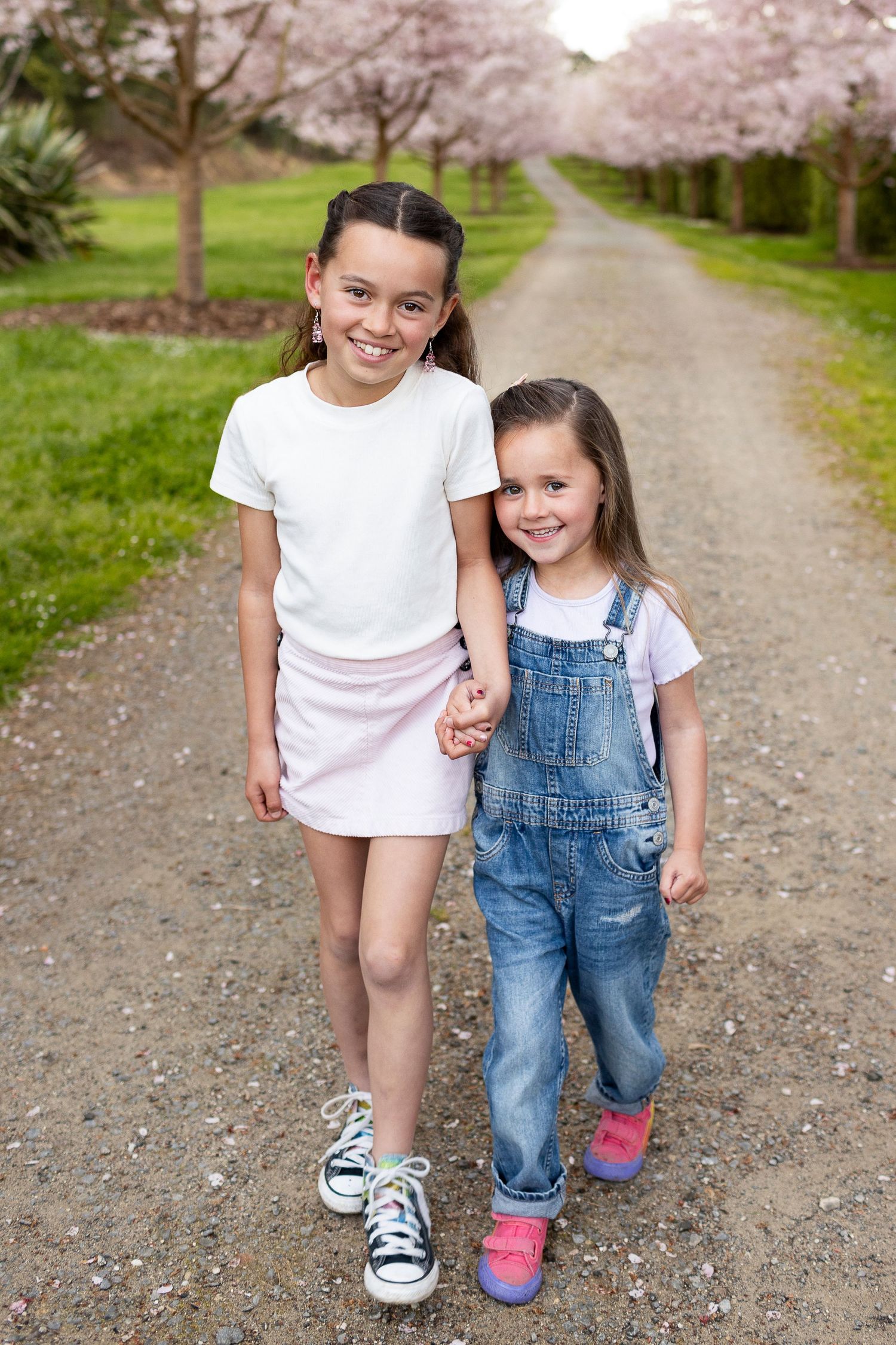 Two children stand together on a path lined with blooming cherry trees in springtime.