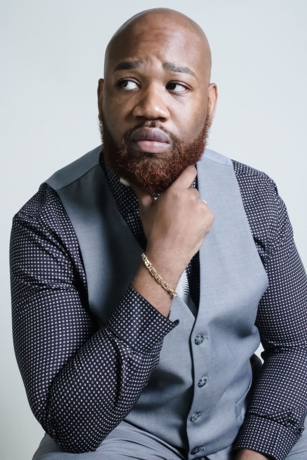 Professional portrait of person in vest and patterned shirt with thoughtful expression.