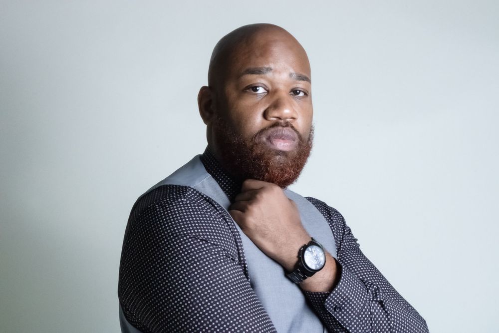 Professional portrait of person in business attire wearing watch against light background.