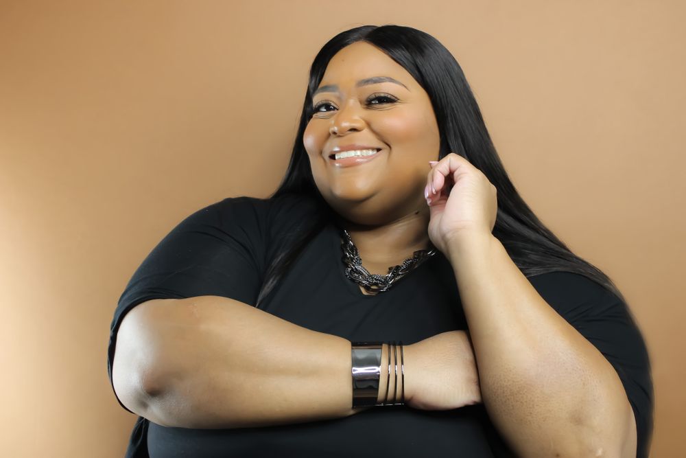 Portrait of person smiling while wearing black outfit and bracelet against warm brown background.