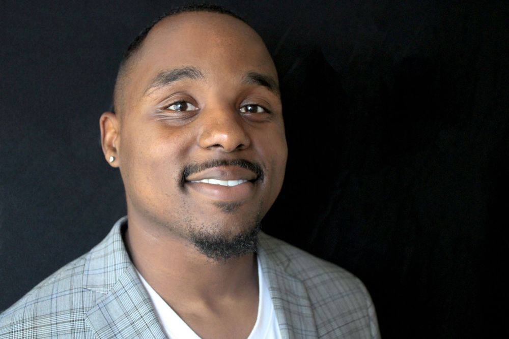 Professional headshot of person in grey blazer smiling against dark background.