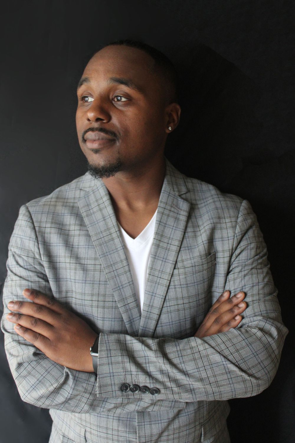 Portrait of person in grey plaid blazer with arms crossed against dark backdrop.