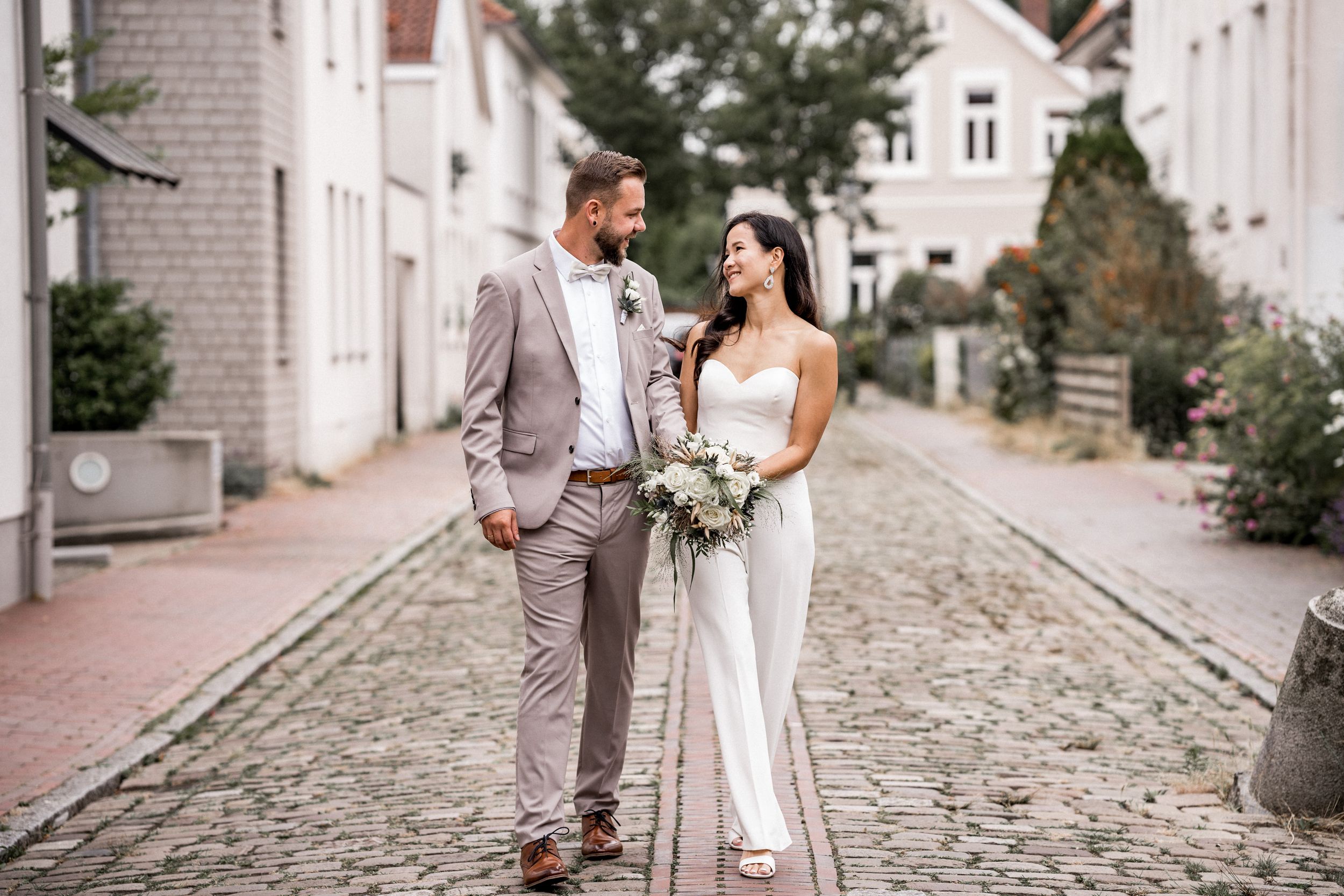 Elegant couple in wedding attire walking on cobblestone street.