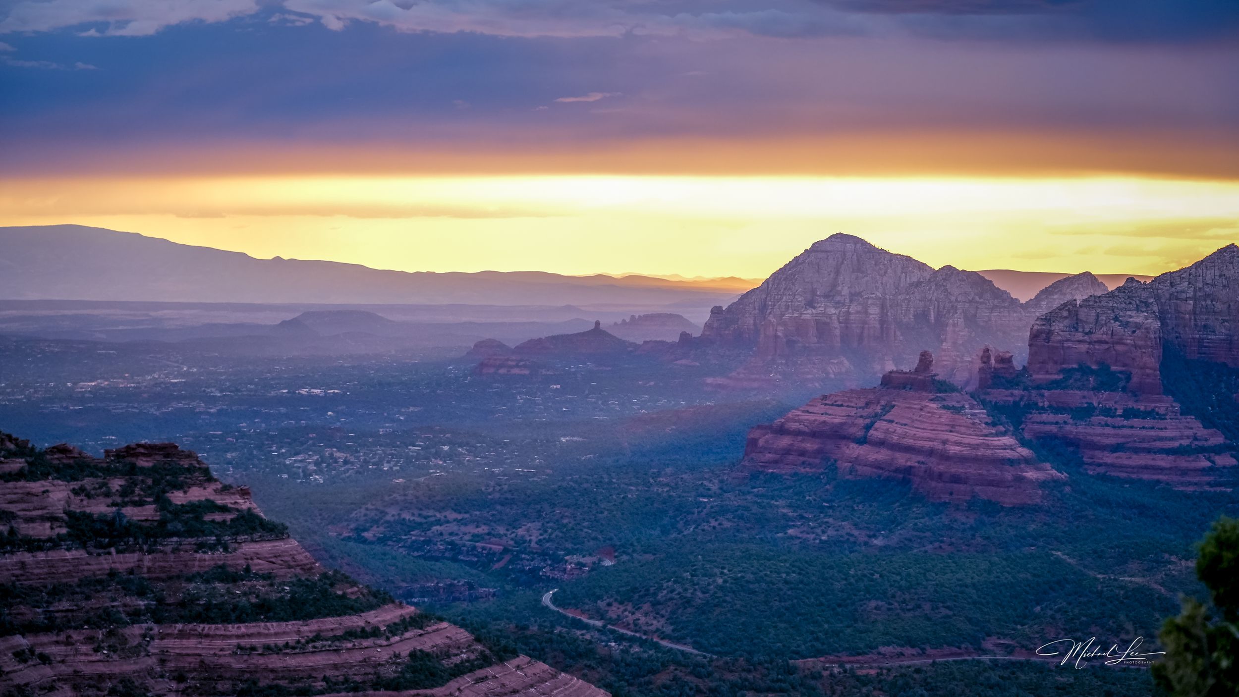 Sunset view over Sedona's red rock formations with mountains silhouetted against golden sky.