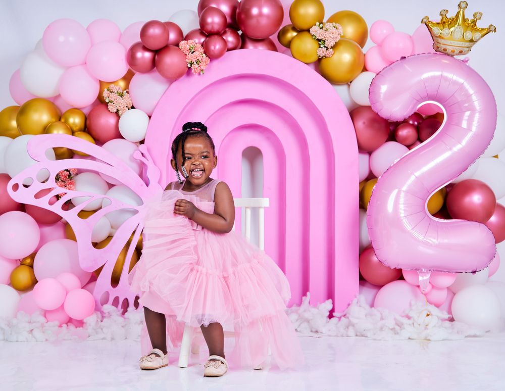 Festive pink balloon arch display with gold accents and crown decorations.