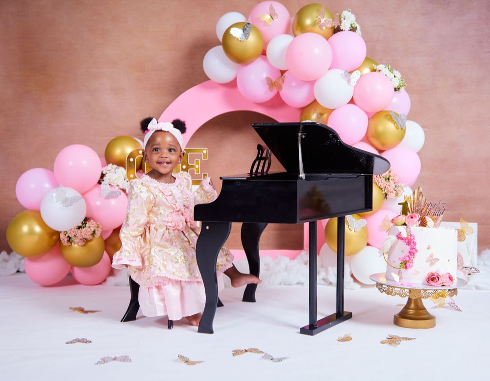 Elegant party setup with pink balloon garland and black piano against rose gold backdrop.