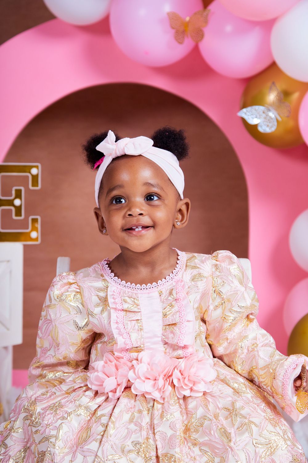 Pink and gold balloon arch decorates a birthday photoshoot setup with elegant decor.