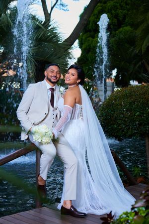 Wedding couple poses near outdoor fountain in garden setting.