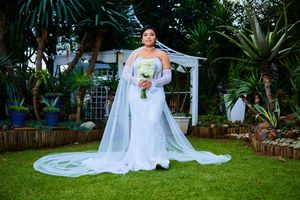 Bride in white gown poses in garden setting with white pergola.