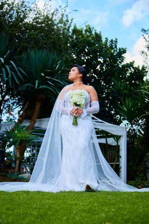 Wedding photography session in lush garden with white pergola and flowing veil.