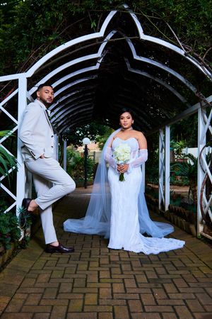 Playful wedding couple poses under garden arch on brick pathway.