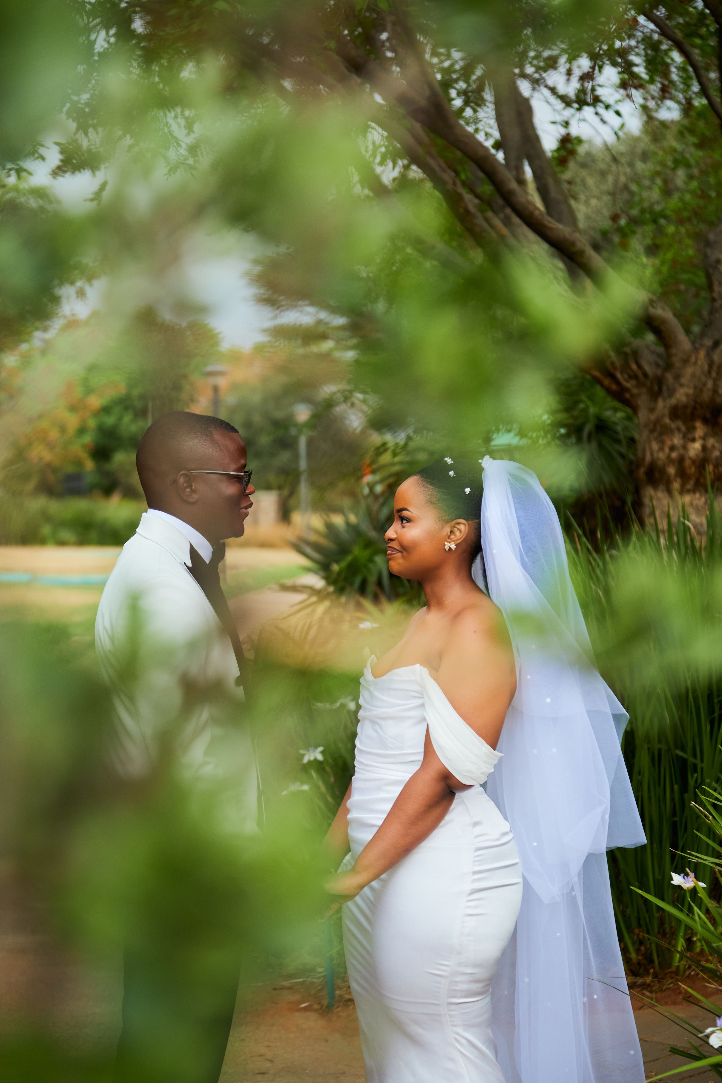 Wedding couple shares romantic moments in a garden setting with soft focus foliage.