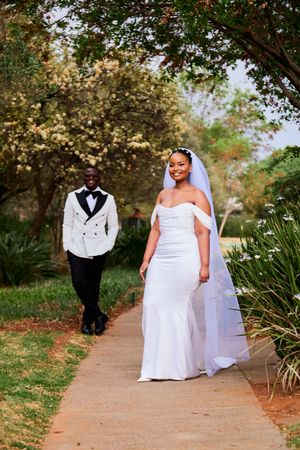 Bride and groom walk along a winding garden path during their wedding photoshoot.