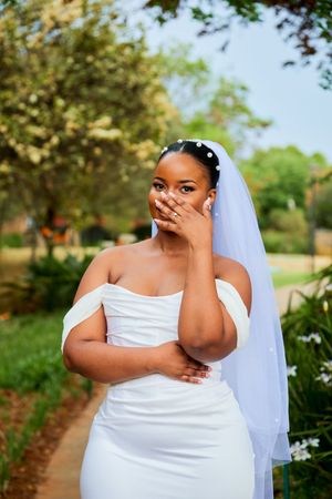 Bride in white dress shows joyful emotion during outdoor wedding photoshoot.