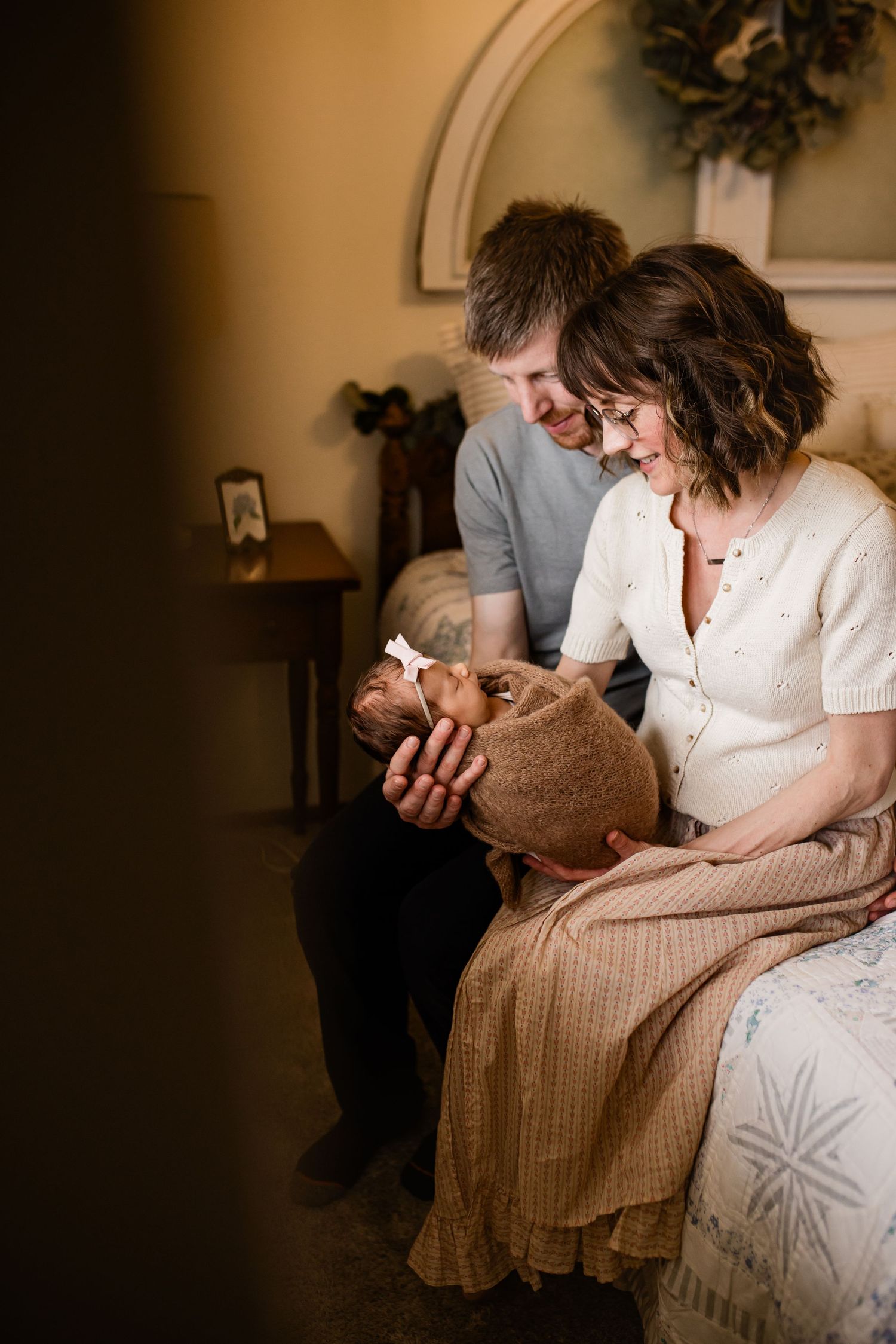 Mom and dad holding baby girl and looking at her lovingly in their home in madison wi during a lifestyle newborn session