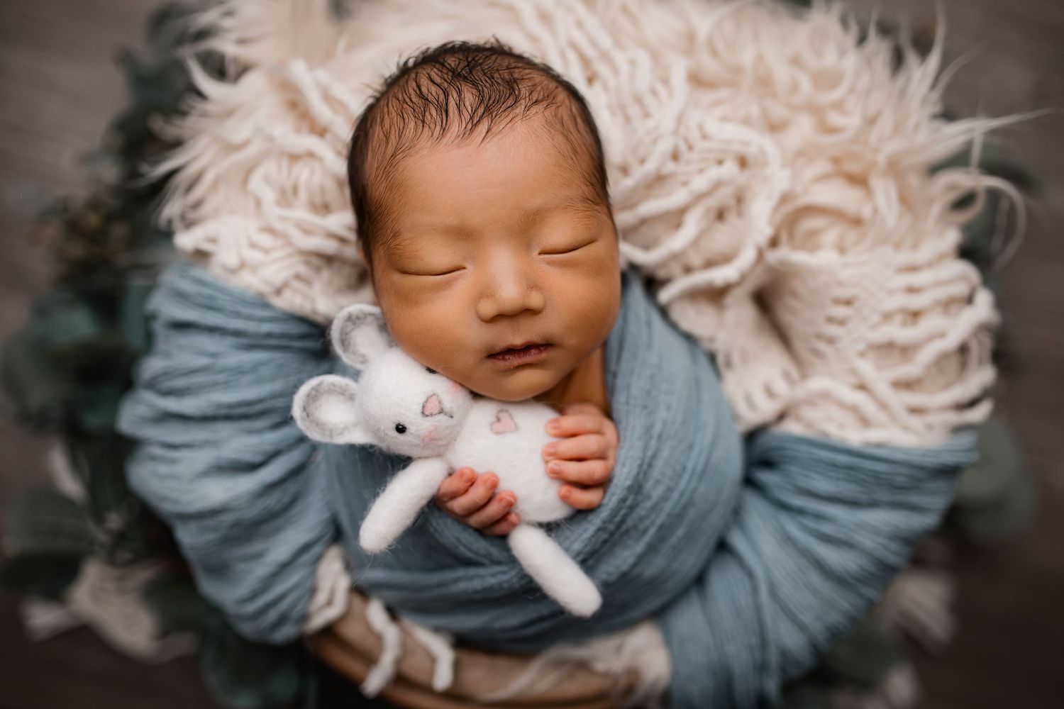 Sweet baby boy asleep in a blue swaddle holding a bunny prop in a newborn studio in Madison WI