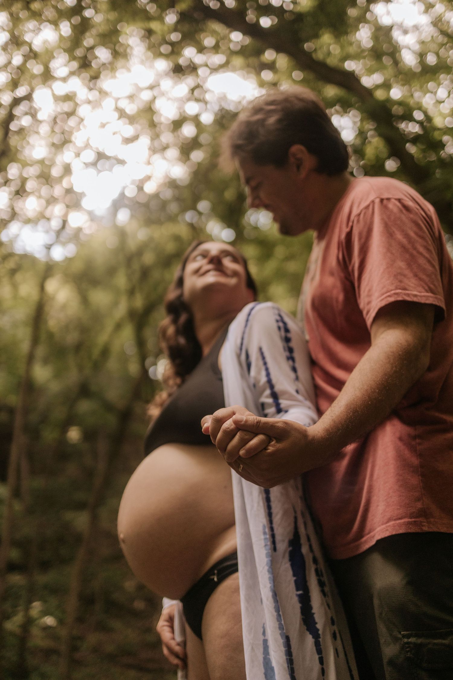 pregnant woman holding hands with her husband in a white kimono, belly exposed and husband standing on her back looking at her