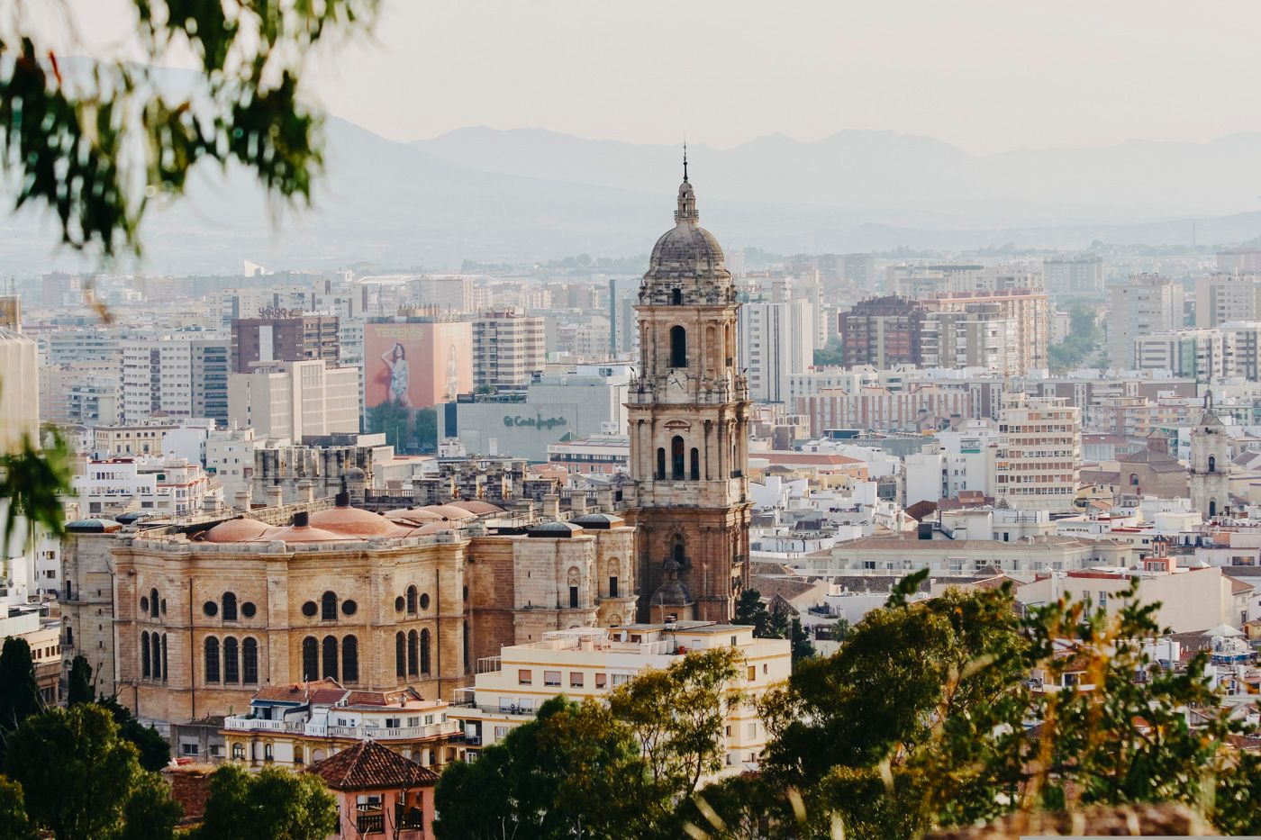 Aerial view of Malaga Cathedral and cityscape with mountains in background under soft daylight.