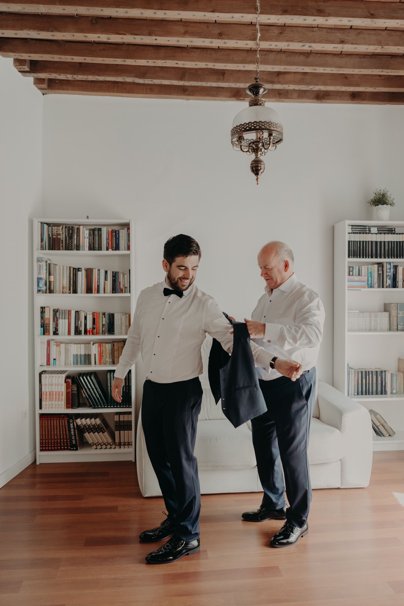 Two men in white shirts reviewing clothing in a room with wooden beams and bookshelves.