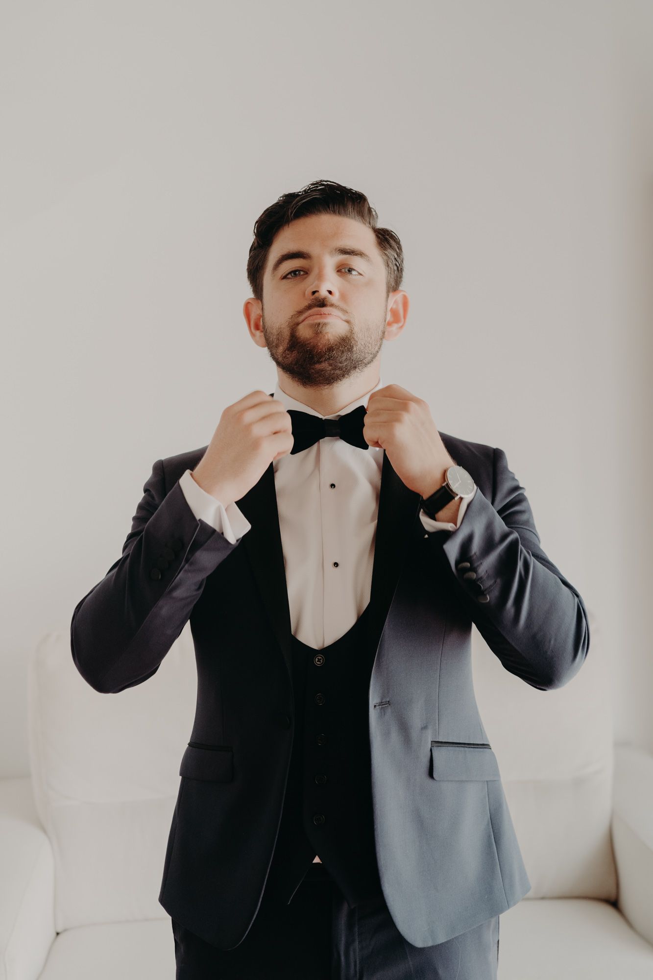 Groom adjusting his bowtie while wearing a classic black tuxedo.