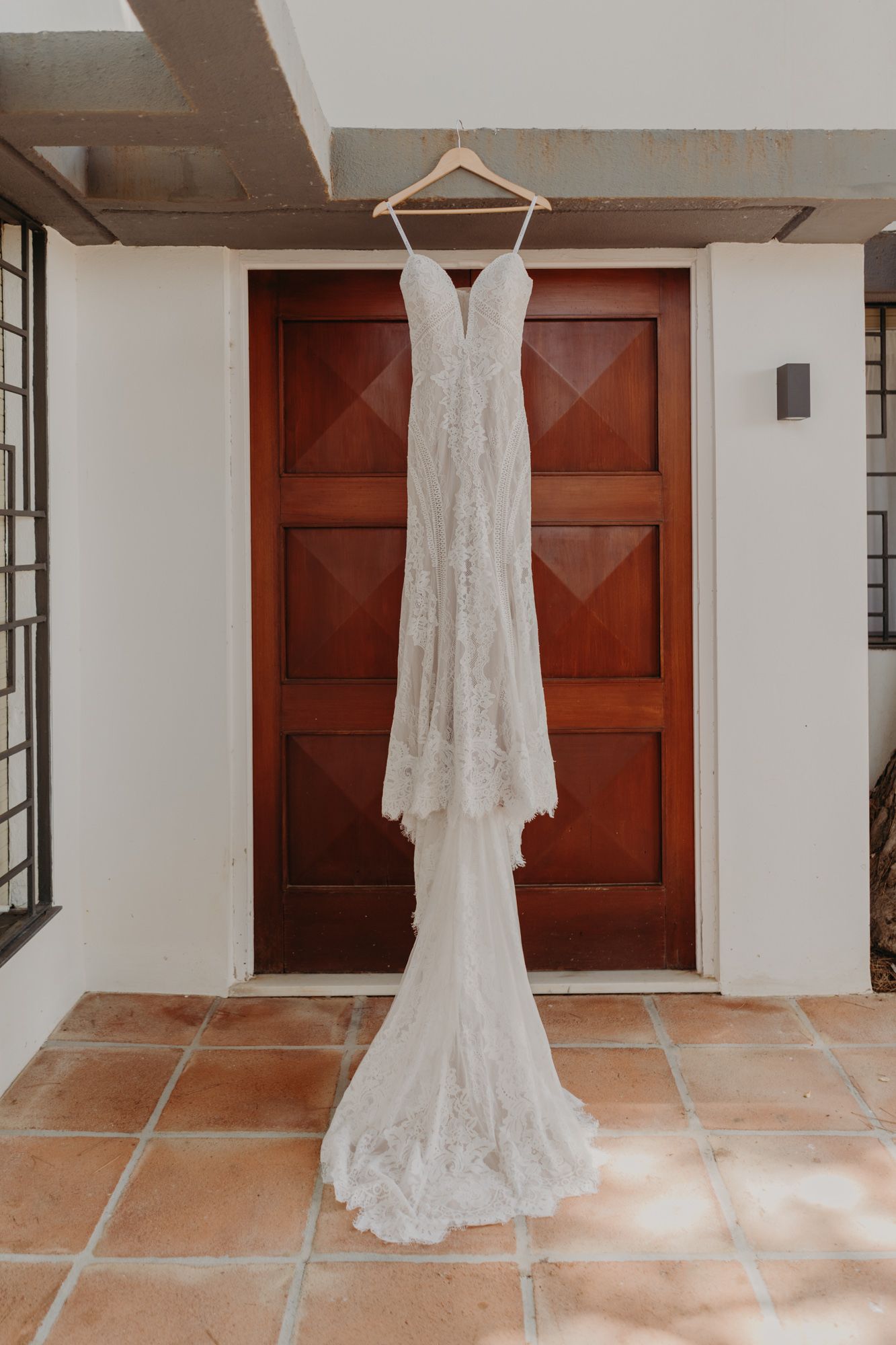 An elegant lace wedding dress hangs on display against a wooden door.
