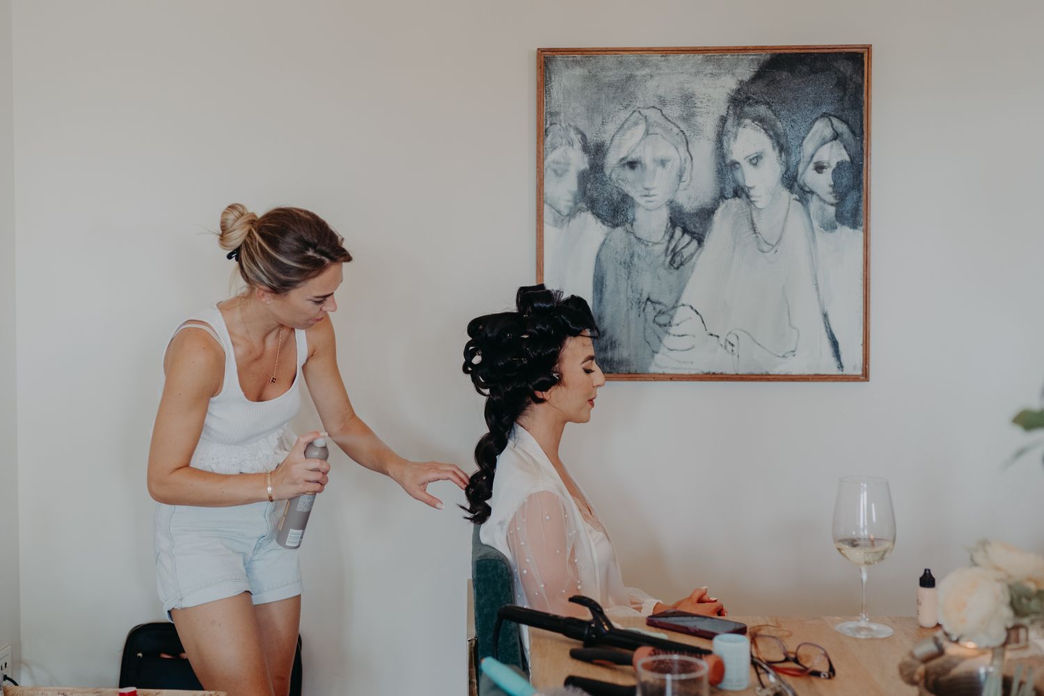Two people getting ready in a casual setting with wine glasses and a framed artwork on the wall.