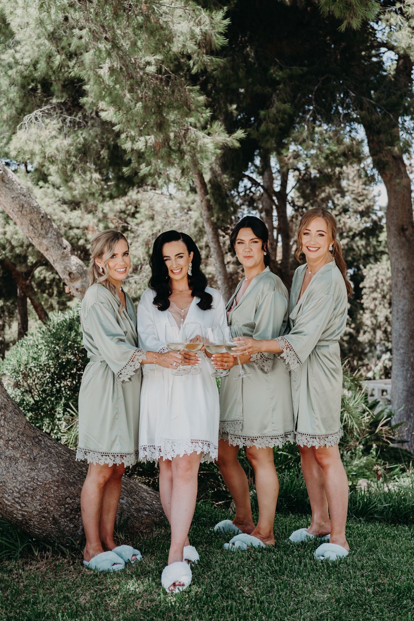 Four people wearing matching robes and slippers pose together in a garden setting.